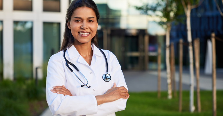 Vrolijke arts staat met haar armen over elkaar buiten voor een ziekenhuis